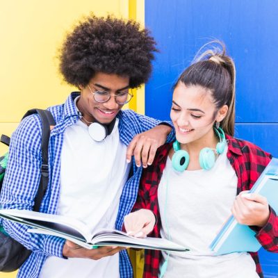diverse-teenage-couple-standing-against-blue-yellow-wall-studying-together